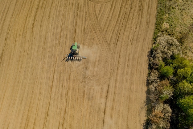 Grande trattore di vista aerea che coltiva un campo asciutto.