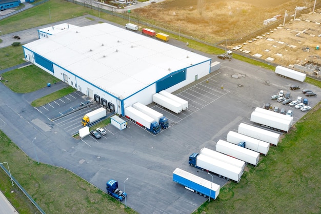 Вид с воздуха на логистический парк со складом, грузовики с прицепами стоят на стоянке и ждут разгрузки и погрузки