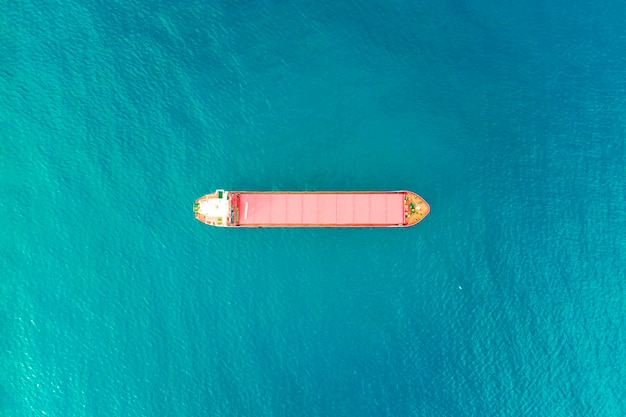 青い海水の背景で航海する孤独なコンテナ船の空中写真 水輸送と物流の概念 上から撮影された貨物を載せた赤いボート 海上配送の航海ビジネス