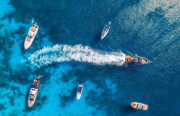 夏の晴れた日の青い海にある高級ヨットやボートの空撮イタリア・サルデーニャ旅行スピードボートヨットの上からのドローンビュー海湾岩だらけの海岸透明な紺碧の水海景