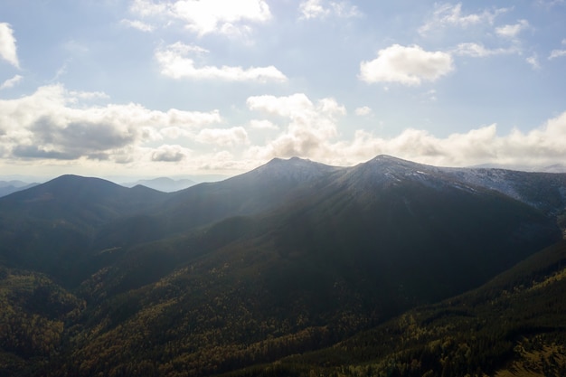 Aerial view of majestic mountains covered with green spruce forest and high snowy peaks.