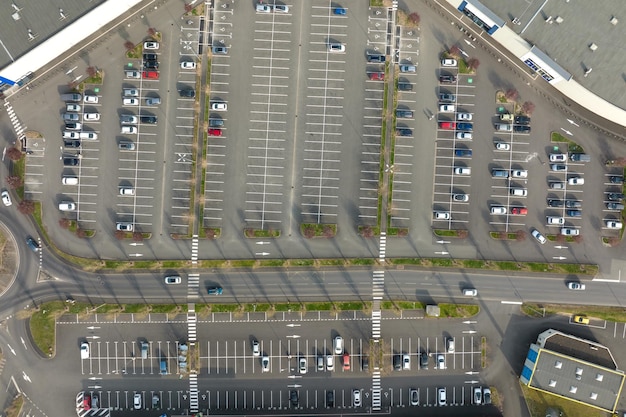 駐車場に駐車されている多くのカラフルな車の航空写真。駐車場所と方向の線とマーキングがあります。