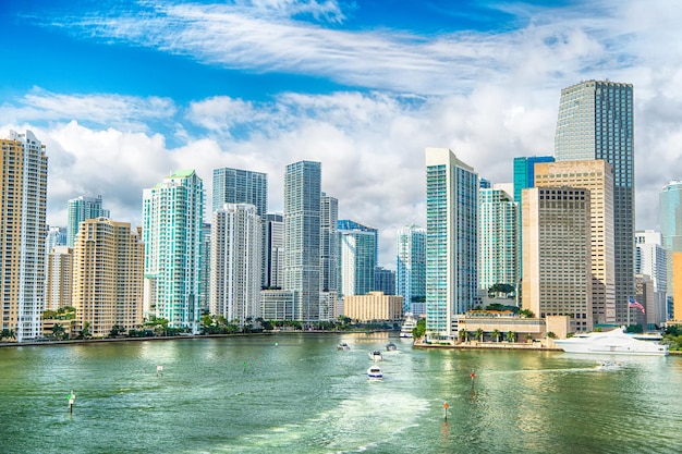 Aerial view of Miami skyscrapers with blue cloudy sky, white boat sailing next to Miami downtown. miami luxury property, modern buildings and yachts