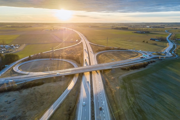 Aerial view of modern highway road intersection at dawn on rural landscape and raising sun background. Drone photography.