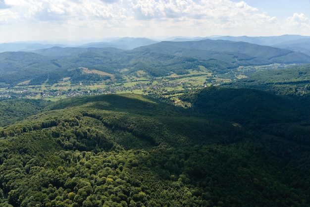 Aerial view of mountain hills covered with dense green lush woods on bright summer day.