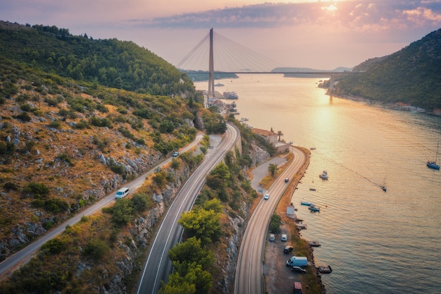 Foto vista aerea di strade di montagna e bellissimo ponte al tramonto dubrovnik croazia vista dall'alto di barche da strada yacht alberi verdi paesaggio estivo con porto mare costa autostrada e cielo nuvoloso