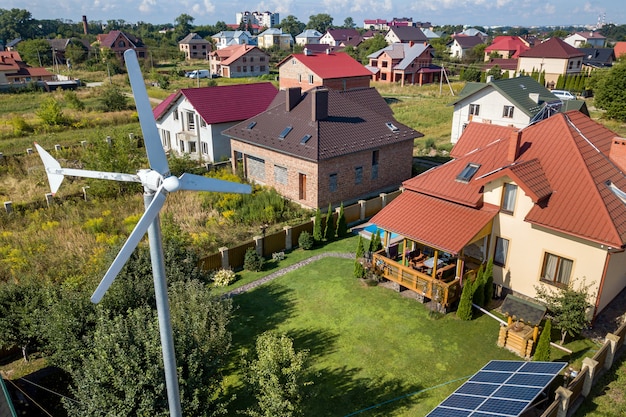 Aerial view of a new autonomous house with solar panels, water heating radiators on the roof and wind powered turbine on green yard.