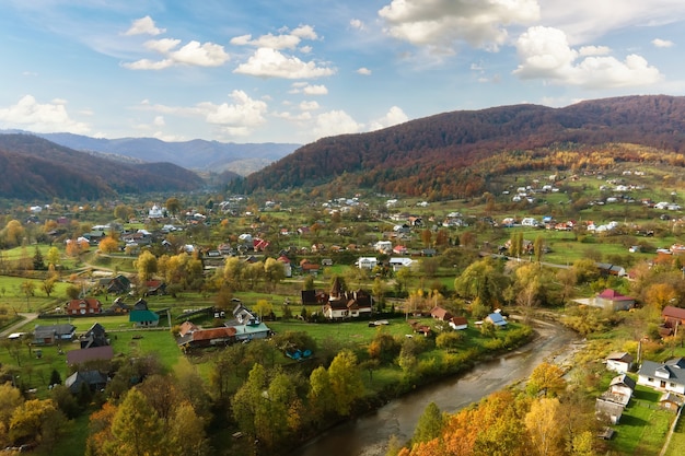 写真 黄色と緑の松の木で覆われた秋の山の丘の間に小さな家がある田舎の村の空撮。