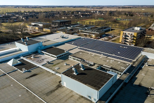 Вид с воздуха на голубые фотоэлектрические солнечные панели, установленные на крыше промышленного здания для производства экологически чистой электроэнергии. производство концепции устойчивой энергетики.
