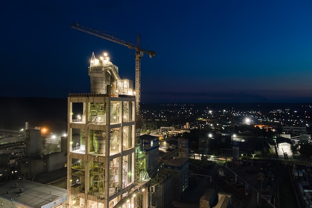 Вид с воздуха на цементный завод с высокой структурой бетонного завода и башенными кранами в производственной зоне в ночное время. производство и глобальная отраслевая концепция.