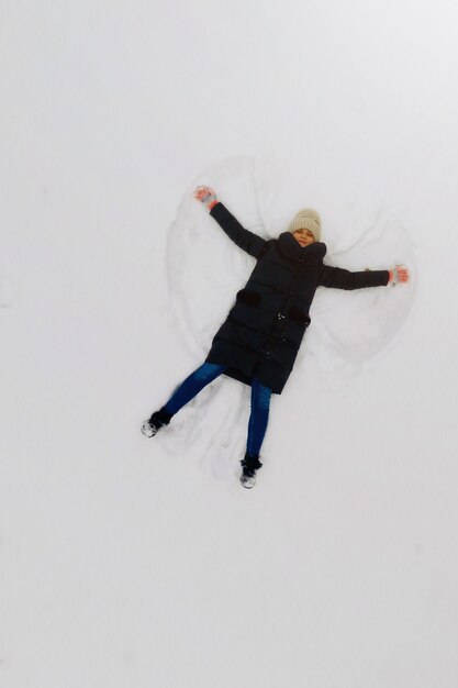 写真 雪の中で若い女性によって作られたスノーエンジェルの空撮。上面図。