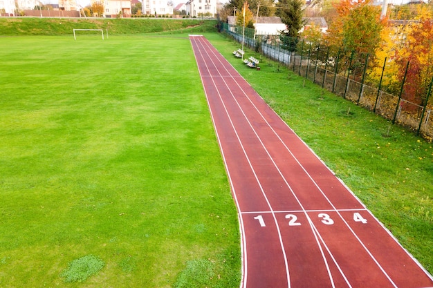 数字が書かれた赤いランニングトラックと緑の芝生のサッカー場があるスポーツスタジアムの空撮。