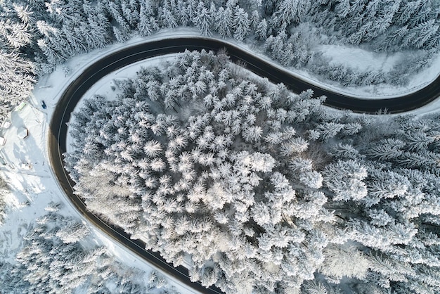 Фото Вид с воздуха на зимний пейзаж с заснеженными горными лесами и извилистой лесной скользкой дорогой.