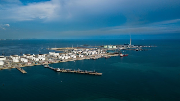 Aerial view oil terminal and coal power plant station in sea\
white oil storage tank chemical petroleum petrochemical refinery\
product tanker ship at deep ocean seaport terminal
