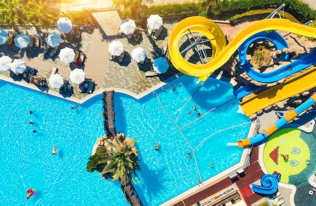 Foto vista aerea del parco acquatico della piscina che nuota persone in acqua blu trasparente ombrelloni lettini alberi verdi al tramonto vacanze estive vista dall'alto del parco acquatico scivoli d'acqua tempo libero in resort di lusso