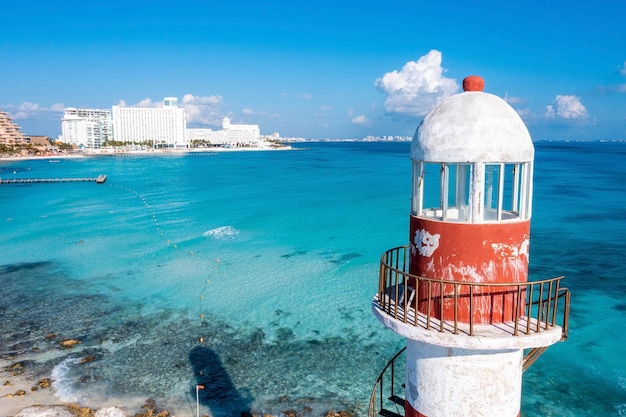 Aerial view of punta cancun lighthouse. the lighthouse adorned with white and red stripes and located in a rocky area