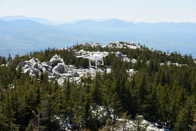 野生の針葉樹の森で覆われた岩山の上を飛んでいるカメラ付き空撮クワッドコプター