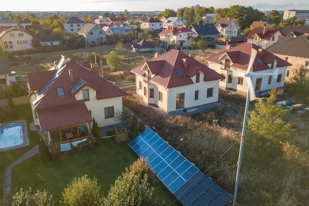 Aerial view of a residential private house with solar panels on roof and wind generator turbine.