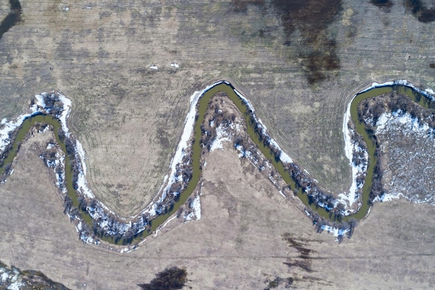 冬の終わりに裸の農地を流れる川の空撮