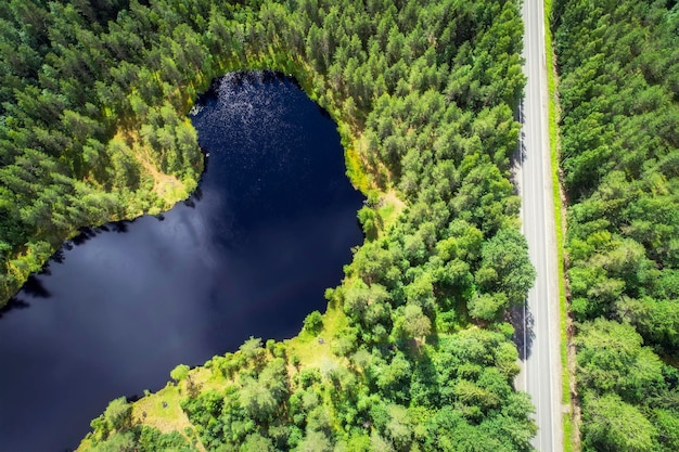 Aerial view of the road between green summer forest and blue lake in Karelia Fishing on the lake with a stop by the road