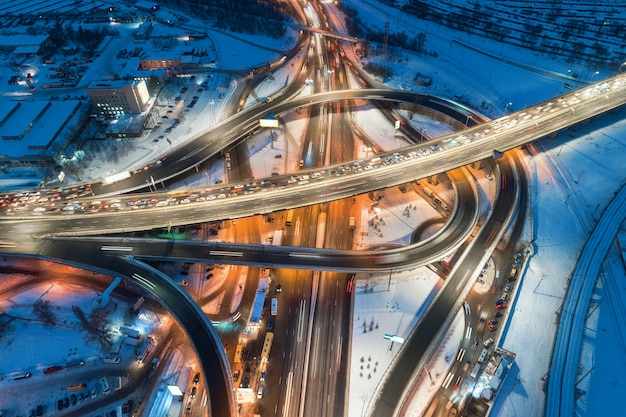 Aerial view of road in the modern city at night in winter. Top view of traffic in highway junction with illumination.