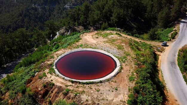 緑の斜面の崖の端にある丸い形の赤い湖の空中景色