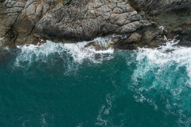 Vista aerea delle onde che si infrangono sul mare onde schiumose bianche sulle rocce in riva al mare vista dall'alto costa rocciosa.