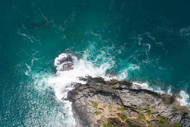 Vista aerea delle onde che si infrangono sul mare onde schiumose bianche sulle rocce in riva al mare vista dall'alto costa rocciosa.