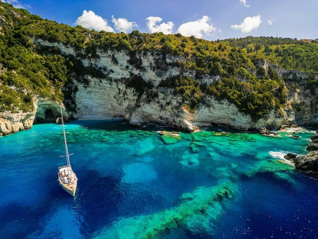 Foto vista aerea di una piccola barca sull'isola di antipaxos con ripide scogliere bianche e grotte in grecia