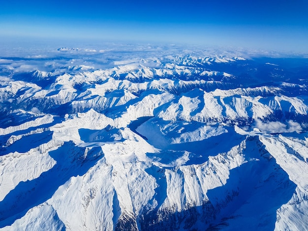 青い空を背景に雪に覆われた山々を空から眺める