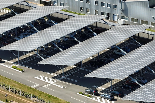 Вид с воздуха на солнечные панели, установленные над парковкой с припаркованными автомобилями для эффективного производства чистой энергии
