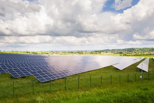 Вид с воздуха на солнечную электростанцию на зеленом поле с забором из проволоки вокруг него. Электрические панели для производства чистой экологической энергии.