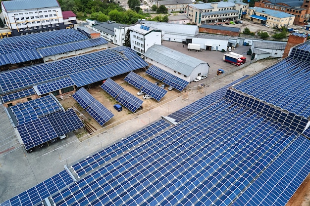 Aerial view of solar power plant with blue photovoltaic panels mounted on industrial building roof for producing green ecological electricity. Production of sustainable energy concept.