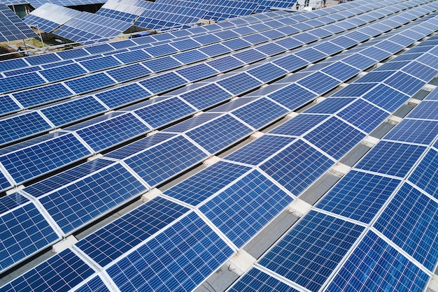 Вид с воздуха на солнечную электростанцию с синими фотоэлектрическими панелями, установленными на крыше промышленного здания для производства экологически чистой электроэнергии. Производство концепции устойчивой энергетики.