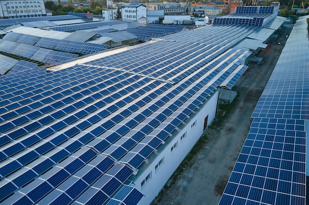 Aerial view of solar power plant with blue photovoltaic panels mounted on industrial building roof for producing green ecological electricity Production of sustainable energy concept