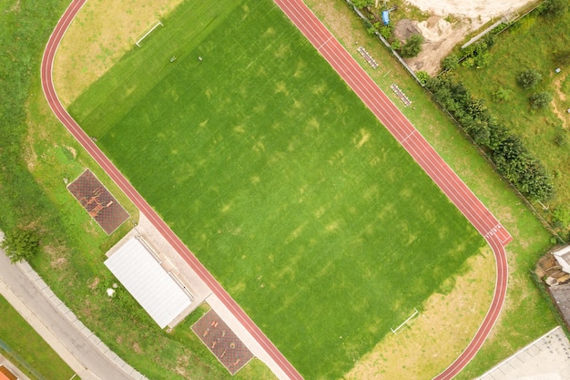 Вид с воздуха на спортивный стадион с красными беговыми дорожками и футбольным полем с зеленой травой.