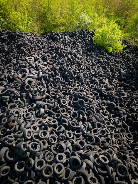 Aerial view of the stark contrast between a massive landfill of used car tires and the surrounding green trees Tire dump showcases human waste impact on environment