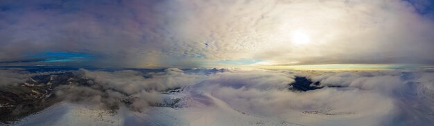 Aerial view of the stunning winter panorama of the snowy slopes and hills among the lush white clouds. The concept of bewitching harsh winter nature