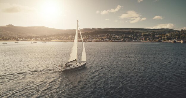 Photo aerial view of sun light on sail boat at ocean bay reflection highland sea coast with forest and