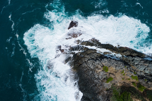 Aerial view Top down seashore big wave crashing on rock cliff Beautiful dark sea surface in sunny day summer background Amazing seascape top view seacoast at Phuket Thailand.