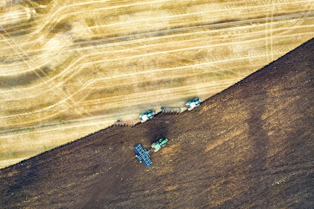 Aerial view of a tractor plowing black agriculture farm field after harvesting in late autumn.