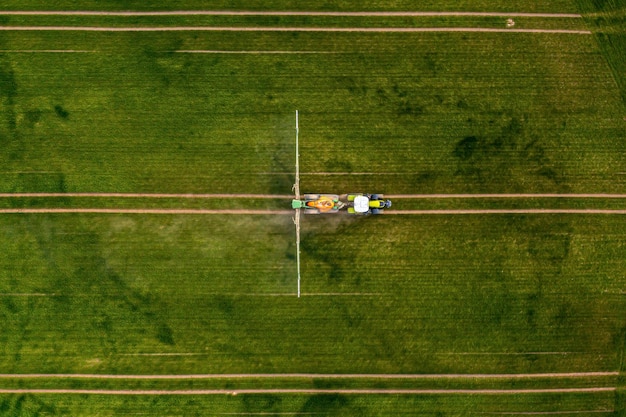 大きな緑の野原に化学物質を噴霧しているトラクターの航空写真