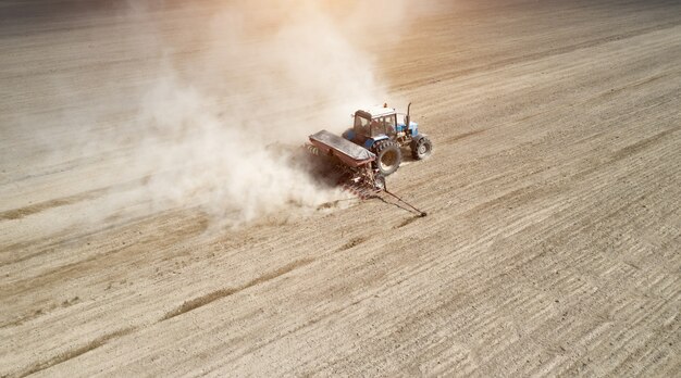 Vista aerea del trattore con la seminatrice montata che esegue semina diretta dei raccolti sul campo agricolo arato. l'agricoltore utilizza macchinari agricoli per il processo di semina, vista dall'alto