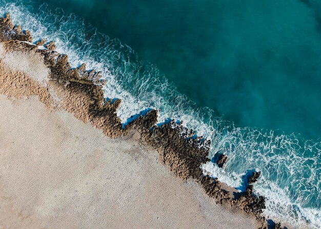 Aerial view of turquoise foam waves hitting the sandy seashore of a Javea coastal town in Spain