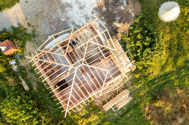 Aerial view of unfinished brick house with wooden roof structure under construction.