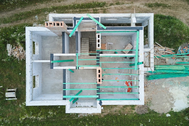 Aerial view of unfinished frame of private house with aerated lightweight concrete walls and wooden roof beams under construction.