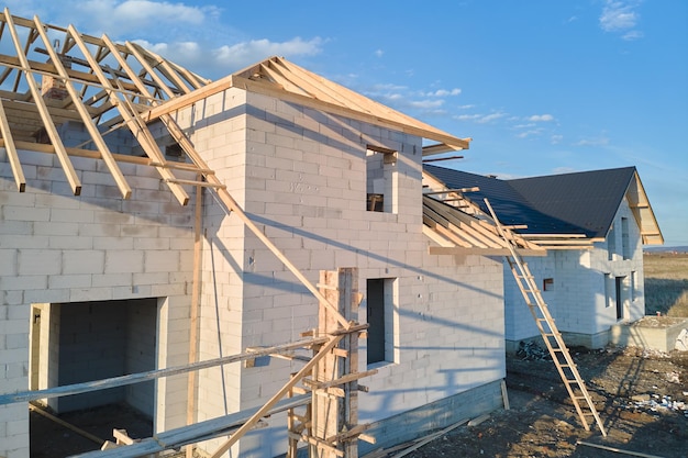 Photo aerial view of unfinished frame of private house with aerated lightweight concrete walls and wooden roof frame under construction.