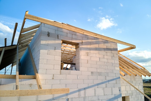 Aerial view of unfinished frame of private house with aerated lightweight concrete walls and wooden roof frame under construction