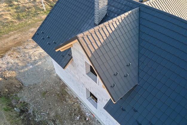 Вид с воздуха на недостроенный дом со стенами из легкого газобетона и деревянным каркасом крыши, покрытым металлической черепицей в стадии строительства