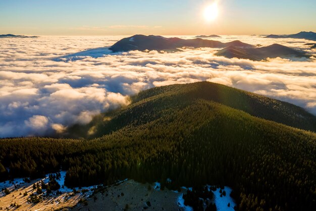 Aerial view of vibrant sunrise over mountain hills covered with evergreen spruce forest in autumn